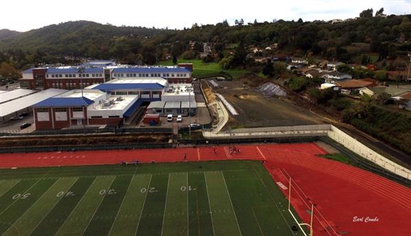 Aerial shot taken from over the football fields showing the progress made in building the retaining wall, maintaining the site, and building the fence in the basketball/tennis courts area.